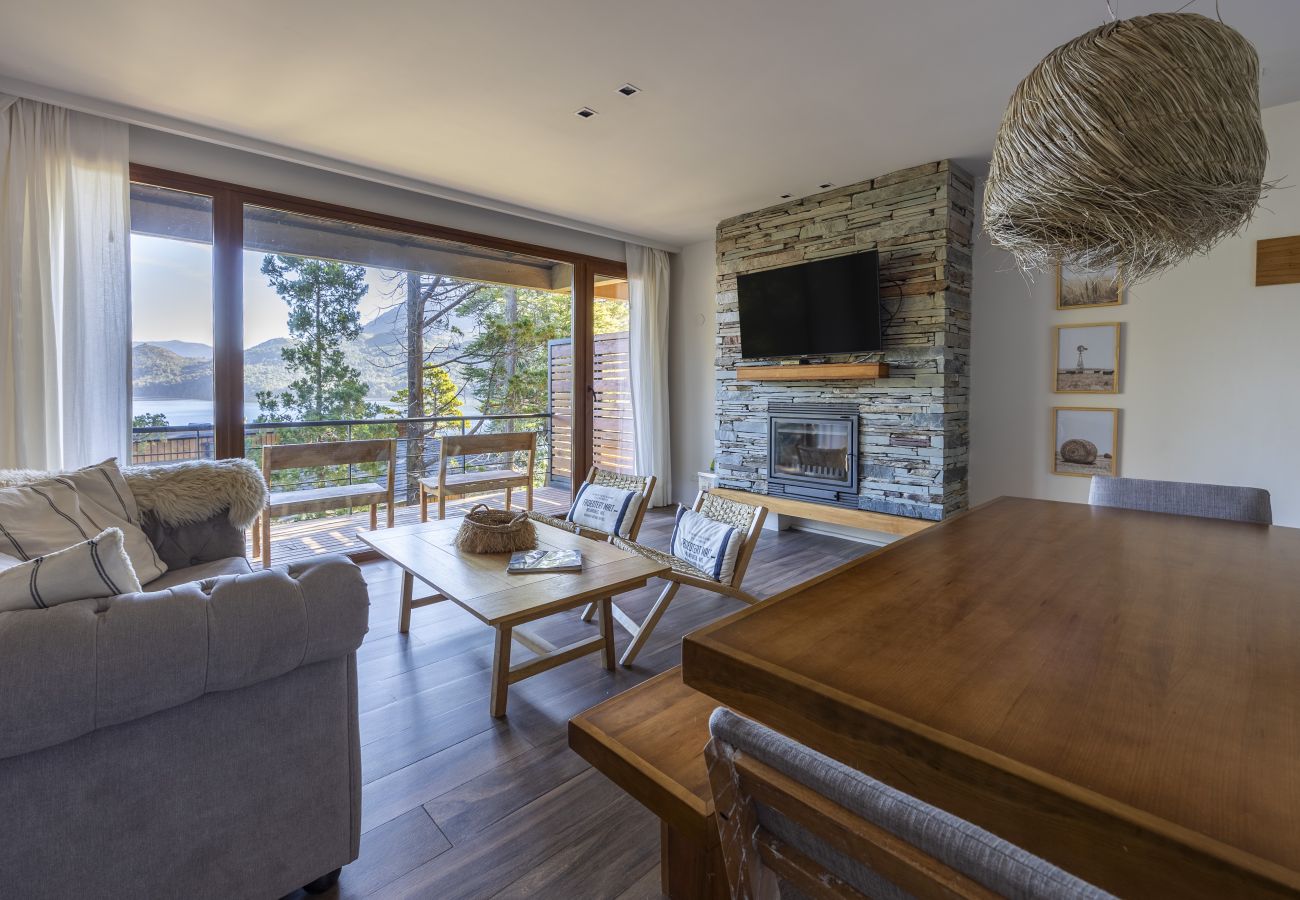 Sala de estar e jantar do apartamento Lenga 1D com lareira Bosca, varanda e vista para o lago.